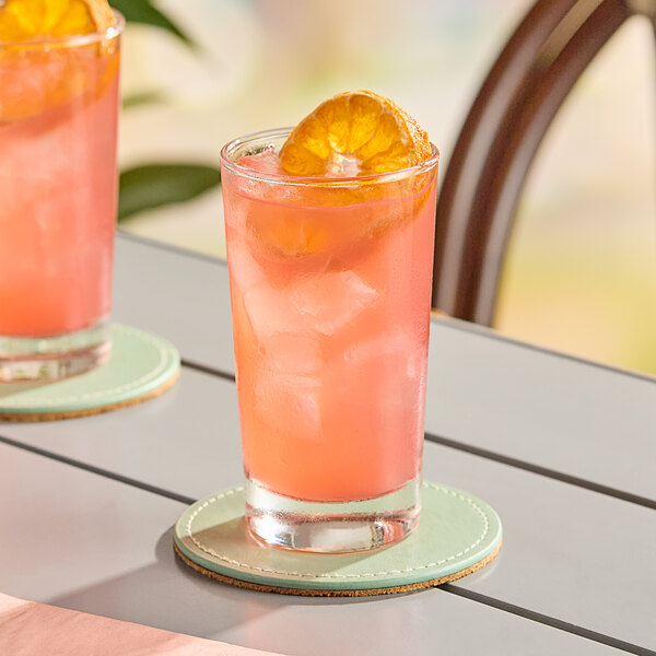 Two Libbey highball glasses filled with pink drinks, ice, and orange slices.