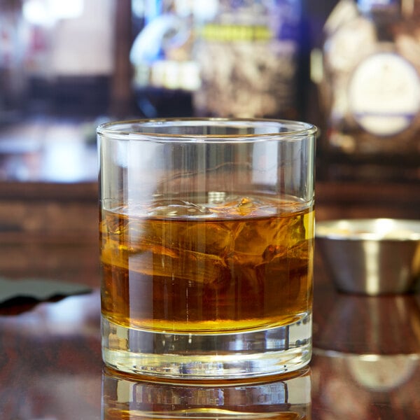 A Libbey rocks glass with a drink and ice on a table.