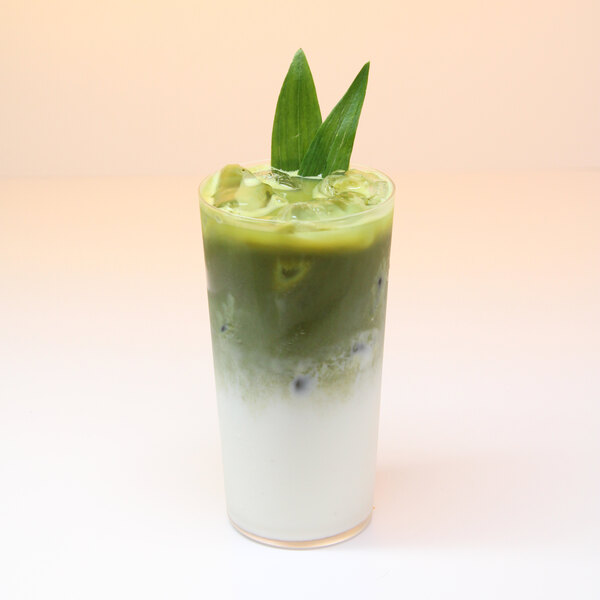 A glass of iced matcha latte with a layer of milk at the bottom and garnished with green leaves.
