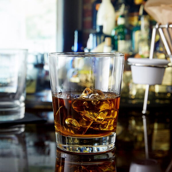 A Libbey double old fashioned glass of brown liquid and ice on a bar counter.