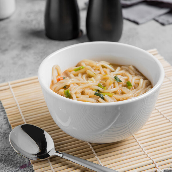 A Libbey Porcelana white porcelain noodle soup bowl with noodles and a spoon.