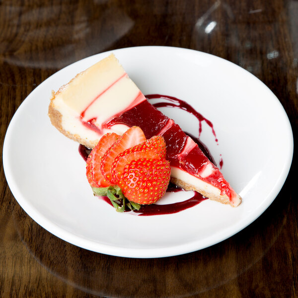 A slice of cheesecake with strawberries on a Libbey Porcelana round white coupe plate.