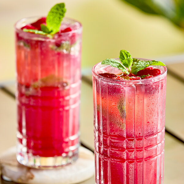 Two glasses of red raspberry drinks with mint leaves on a table.