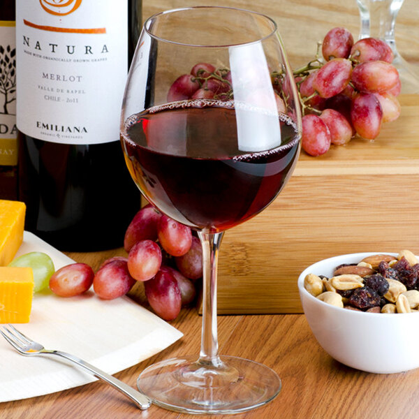 A Libbey balloon wine glass filled with red wine and grapes on a table.