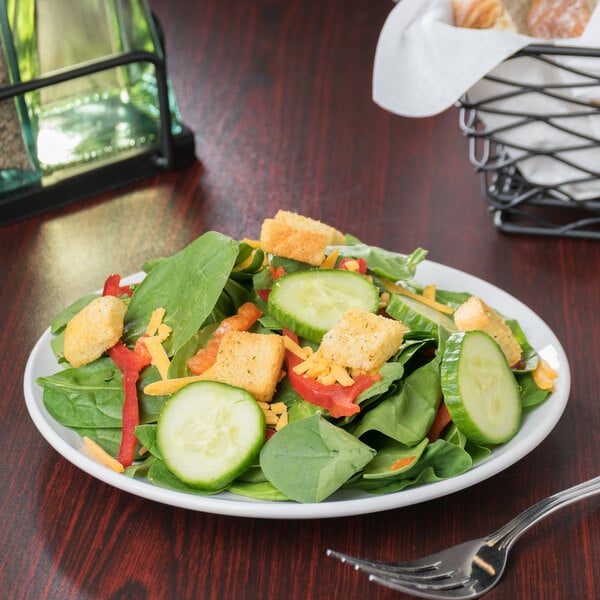 A Libbey Porcelana round coupe plate with a salad with croutons, cucumbers, and green peppers.