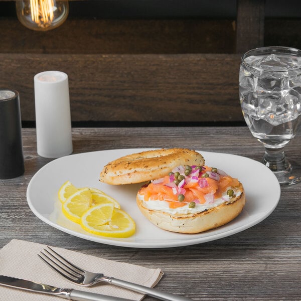 A Libbey Porcelana bright white porcelain plate with a bagel and salmon with lemon slices.