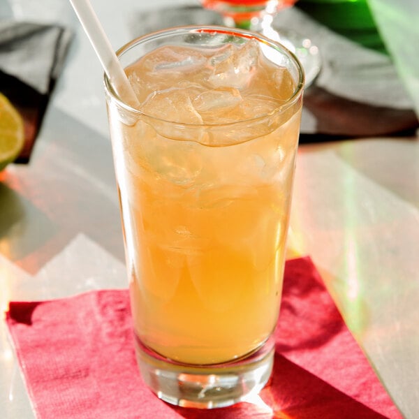 A Libbey highball glass of orange liquid with ice and a straw.