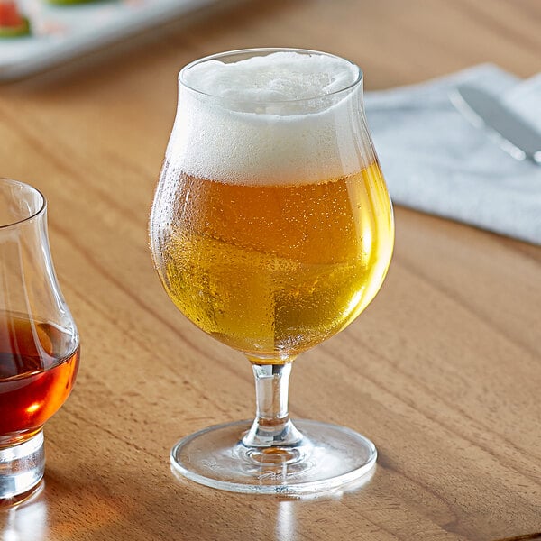 A Reserve by Libbey Belgian beer glass full of beer with foam on a table.