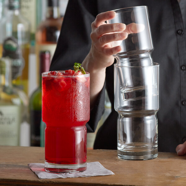 A person pouring a red drink into a Libbey Newton Stackable Beverage Glass on a table.