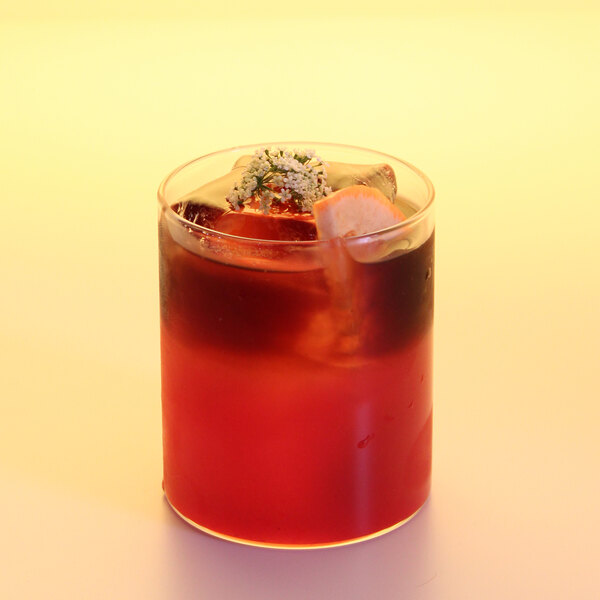 A glass of red blood orange beverage with ice and a garnish on top.