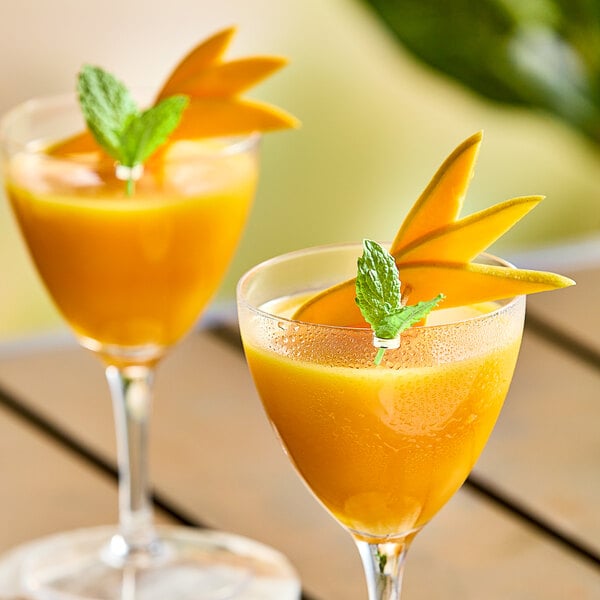 Two glasses of mango juice with mint leaves on top on a table.