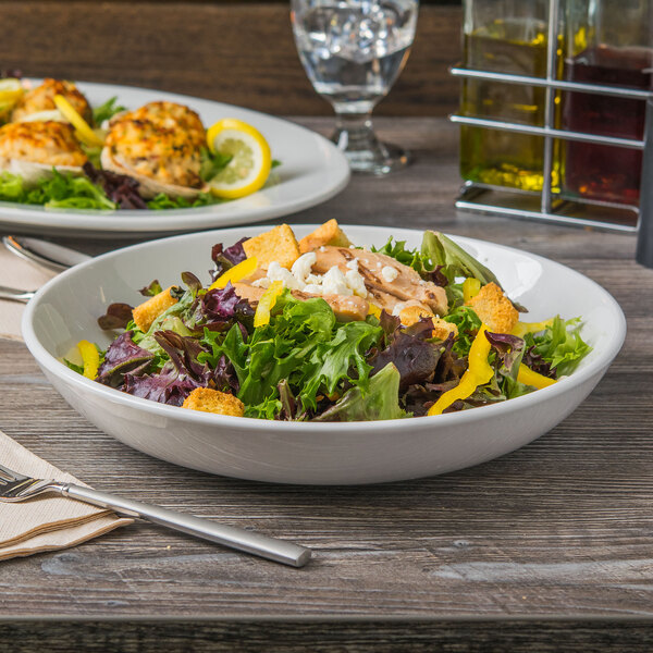 A salad in a Libbey bright white porcelain low bowl on a table with a glass of wine.