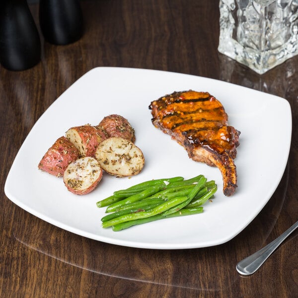 A Libbey Porcelana coupe plate with steak, potatoes, and green beans on a table.