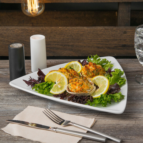 A Libbey Porcelana white triangular coupe plate with food on it on a table with silverware.