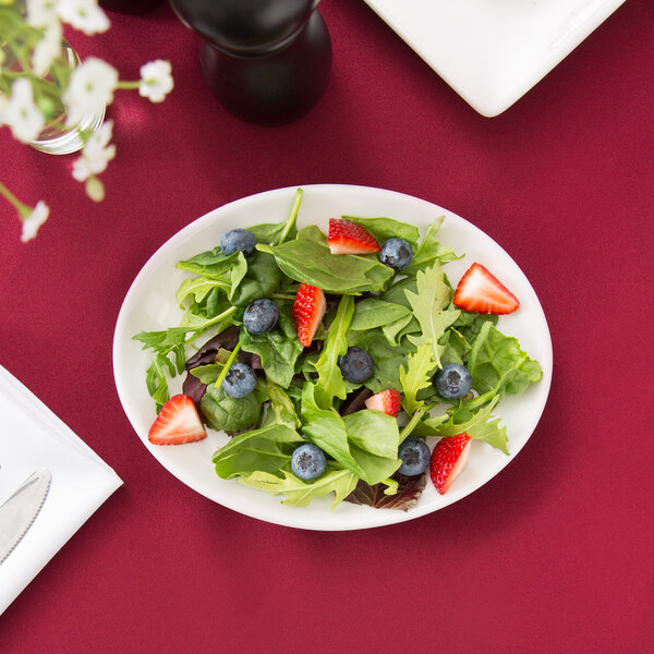 A Libbey white oval platter with a salad of greens, strawberries, and blueberries.