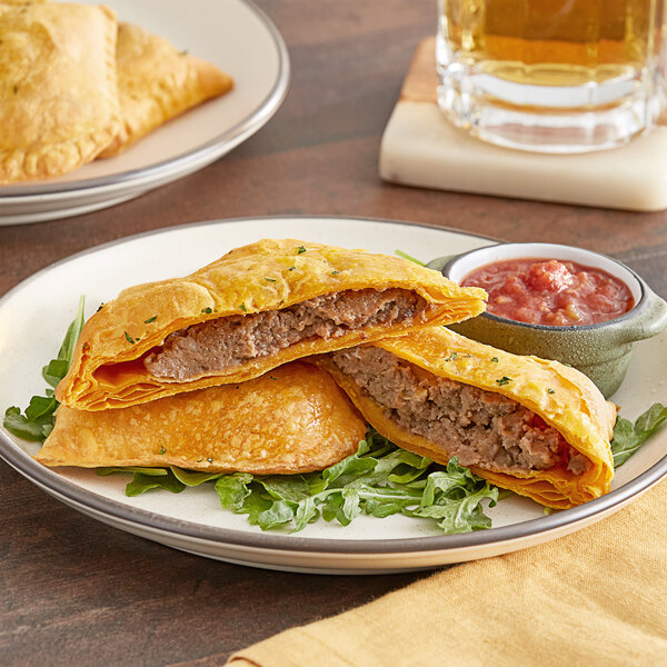 A Caribbean Food Delights Spicy Beef Patty on a plate with a glass of beer.