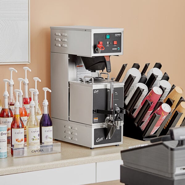 A Curtis Gemini stainless steel analog coffee machine on a counter in a corporate cafeteria.