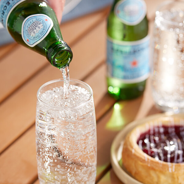 A person pouring San Pellegrino sparkling natural mineral water from a green glass bottle into a glass.