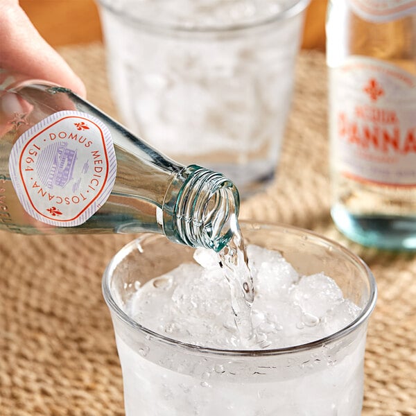 A person pouring Acqua Panna Natural Spring Water from a glass bottle into a glass.