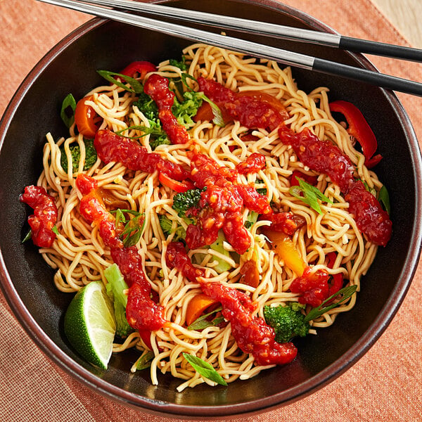 A bowl of noodles with Lee Kum Kee chili garlic sauce and vegetables on a white background.