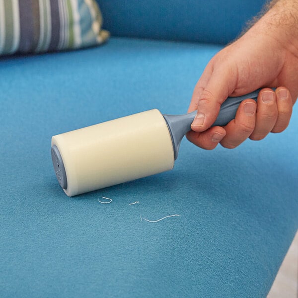 A hand using a 3M Scotch-Brite lint roller to clean a couch.