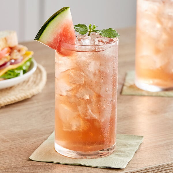 A glass of Tractor Beverage Co. Organic Watermelon Mint drink with a slice of watermelon on the rim.