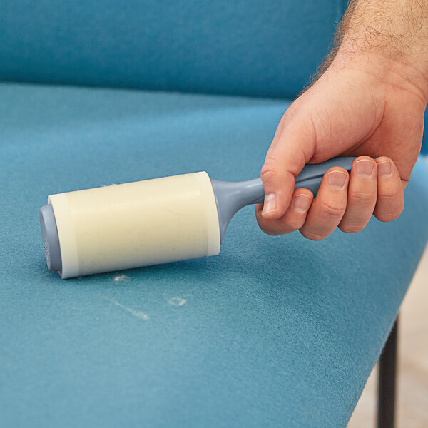 A hand using a 3M Scotch-Brite lint roller to clean a chair.