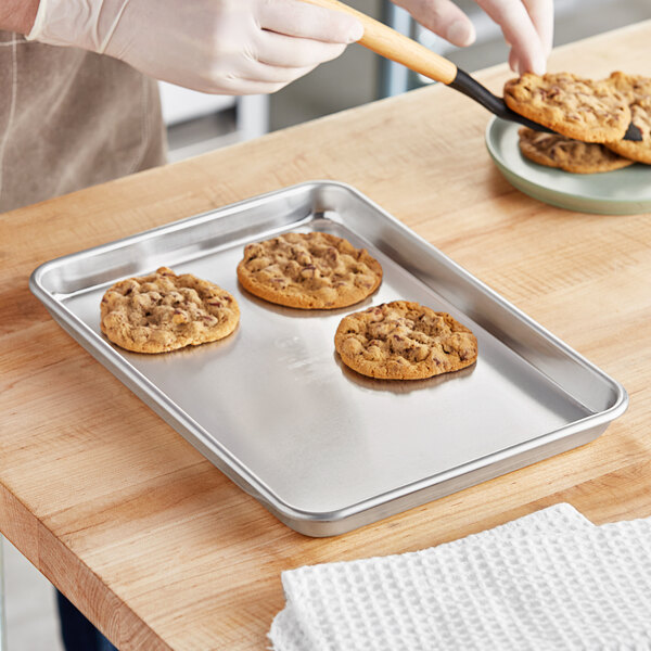 A person using a spatula to cut cookies on a Vollrath bun sheet pan.