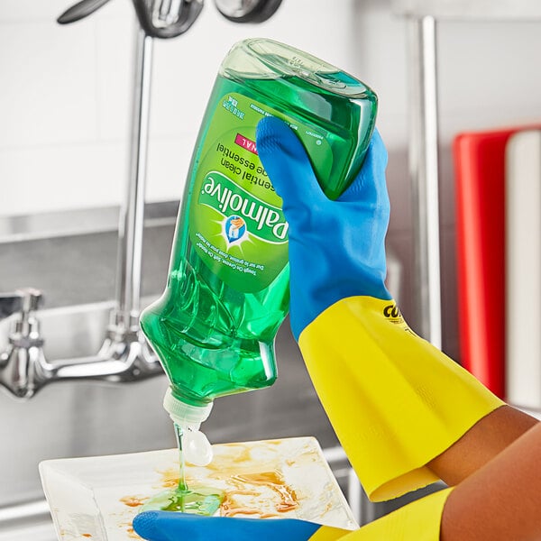 A hand in a yellow rubber glove holding a green bottle of Palmolive Original Scent dish soap.