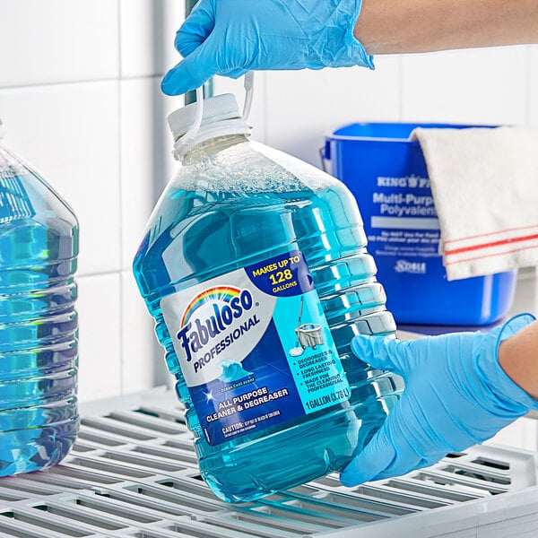 A person in blue gloves holding a large bottle of Fabuloso Ocean Cool all-purpose cleaner.