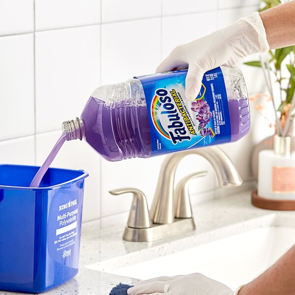 A hand pouring purple Fabuloso multi-purpose cleaner into a blue container.