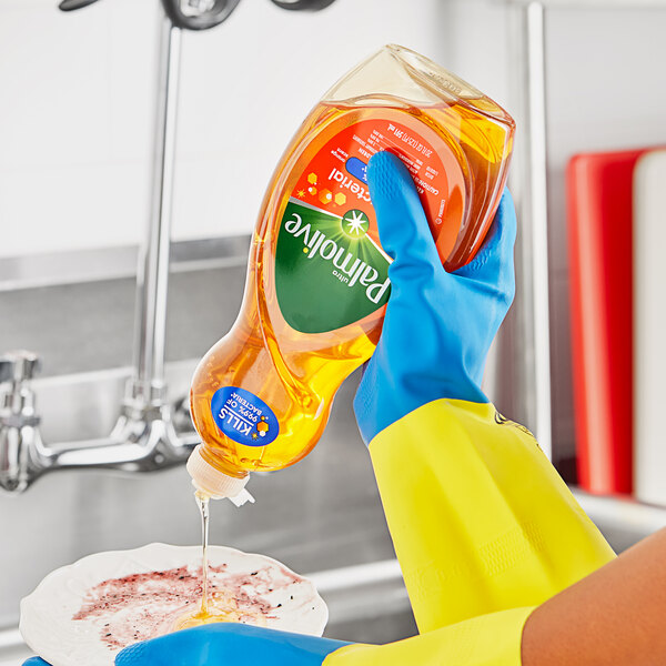 A person in yellow gloves pouring Palmolive dish soap from a plastic bottle into a bowl.