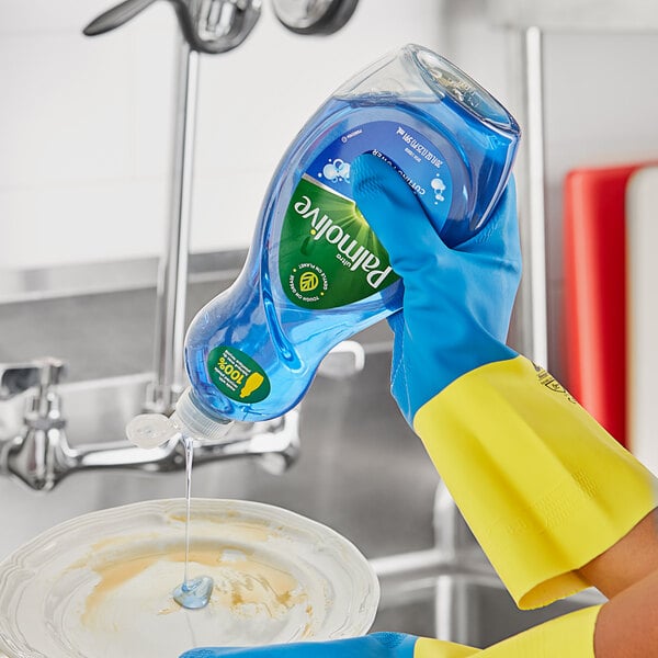 A hand in a yellow glove pours Palmolive dish soap into a bowl on a kitchen counter.