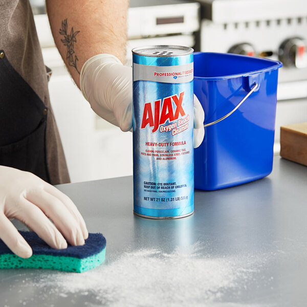 A person in gloves cleaning a counter with a blue can of Ajax powder.