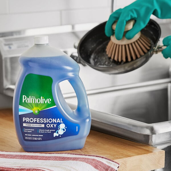 A gloved hand uses Palmolive Ultra Oxy Power Degreaser to clean a pot.