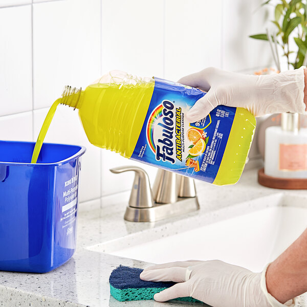 A person pouring Fabuloso Citrus Scent Antibacterial liquid into a blue bucket to clean a sink.