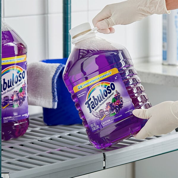 A gloved hand holding a large bottle of Fabuloso lavender-scented liquid.