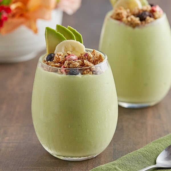 Two glasses of green smoothie with granola and berries on a table.