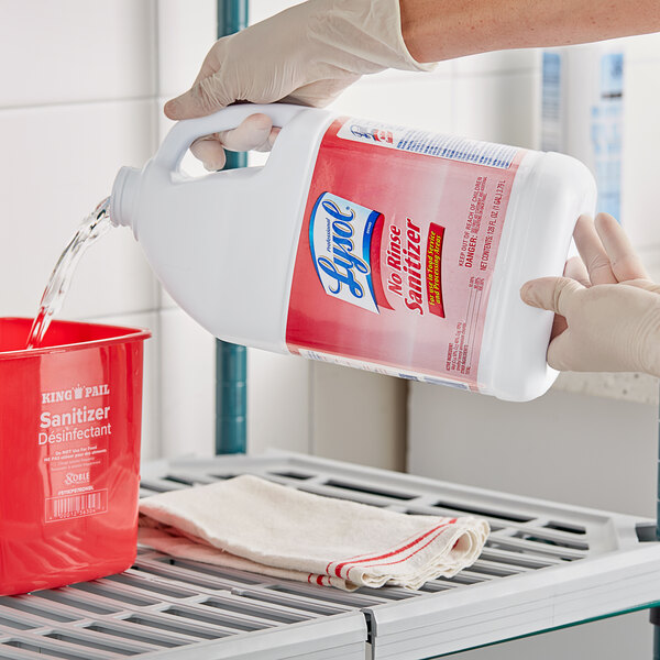 A person pouring Professional Lysol sanitizer into a red container.