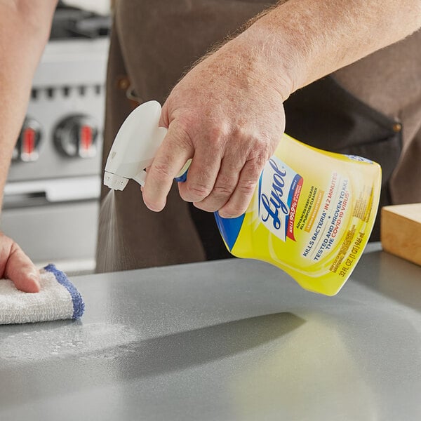 A hand using Lysol Lemon Breeze spray on a counter.