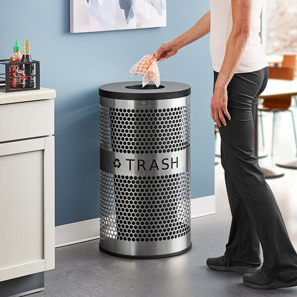 A woman putting a plastic bag in a Lancaster Table & Seating stainless steel perforated trash can.