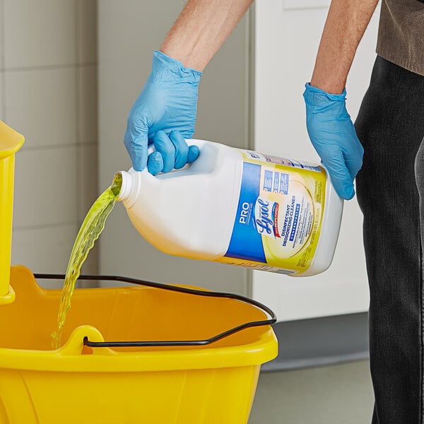 A person in blue gloves pouring yellow Professional Lysol cleaner into a bucket.