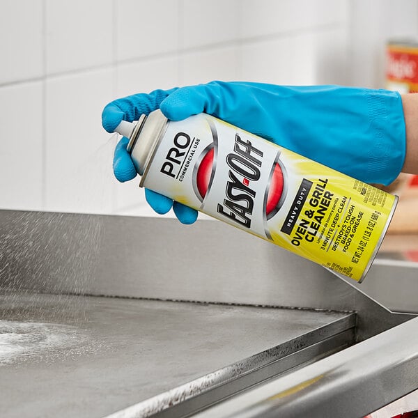 A person in blue gloves spraying Easy-Off Heavy-Duty Oven and Grill Cleaner from a can on a kitchen counter.