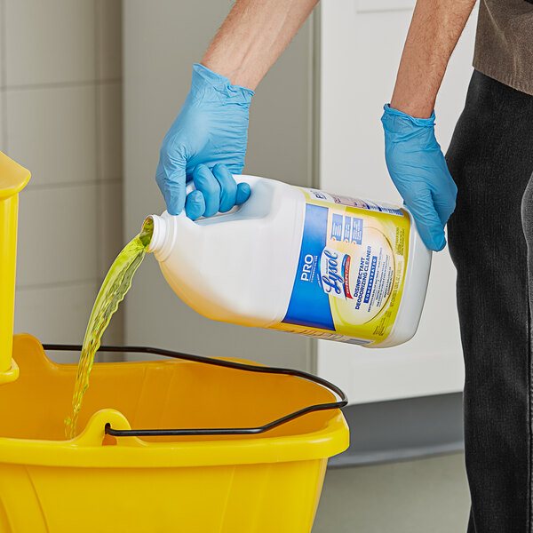A person in blue gloves pouring yellow Lysol cleaner into a bucket.