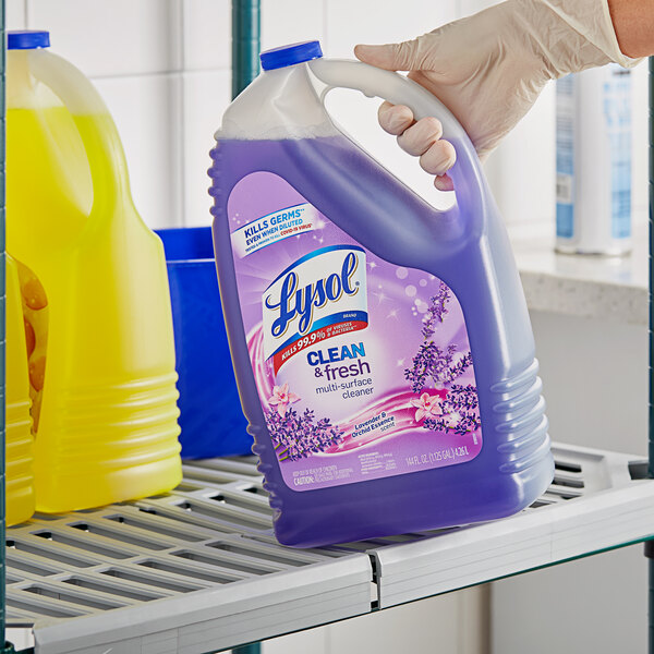 A hand in a yellow glove holding a Lysol Lavender and Orchid Essence Multi-Surface Cleaner bottle.