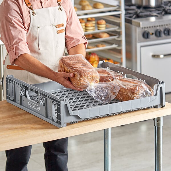 A man in an apron placing loaves of bread in a gray Baker's Lane tray on a bakery counter.