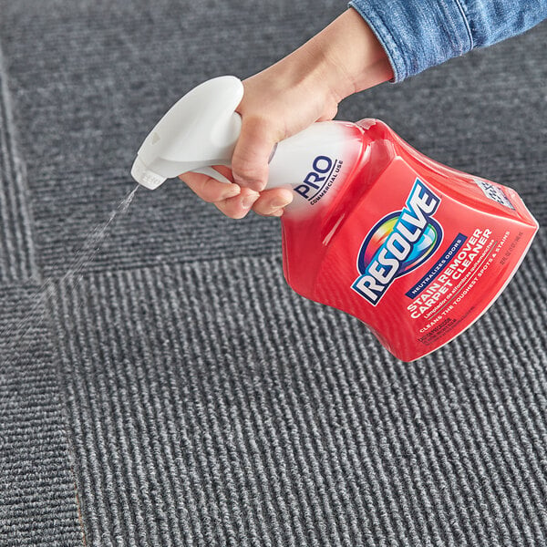 A hand holding a white spray bottle spraying Resolve carpet cleaner on a carpet.