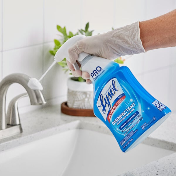 A hand in a glove holding a blue bottle of Professional Lysol Disinfectant Bathroom Cleaner.