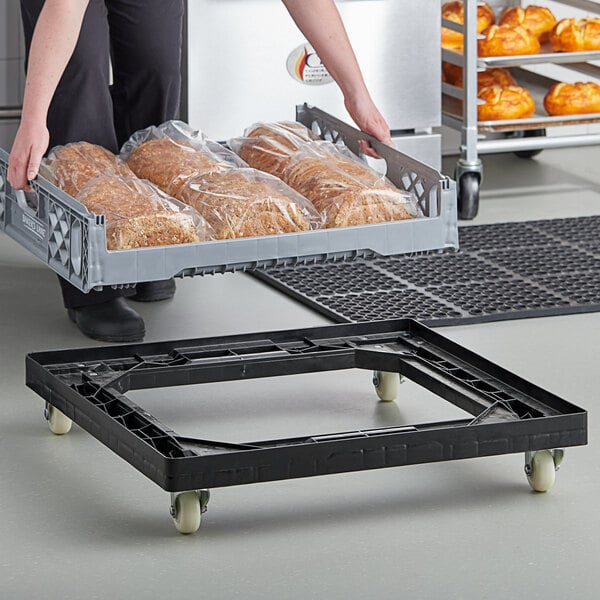 A woman using a black Baker's Lane bread tray dolly to transport bread in plastic bags.