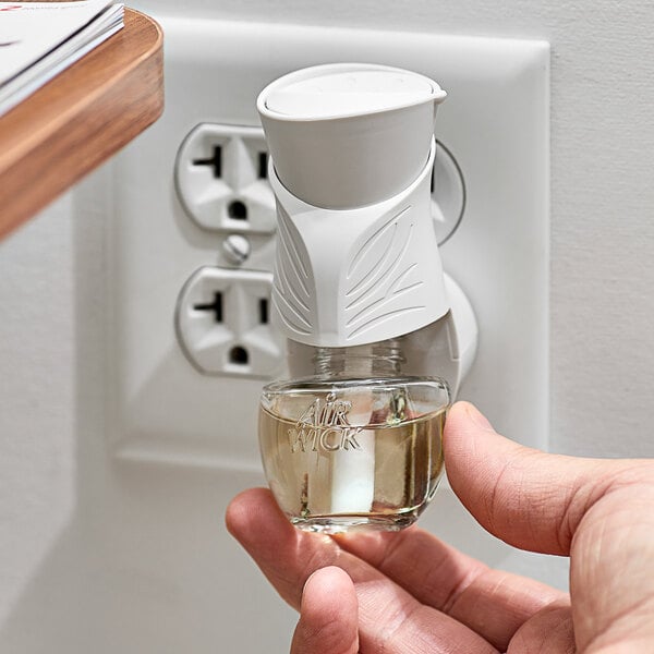 A hand holding an Air Wick Fresh Waters scented oil refill over a wall outlet.